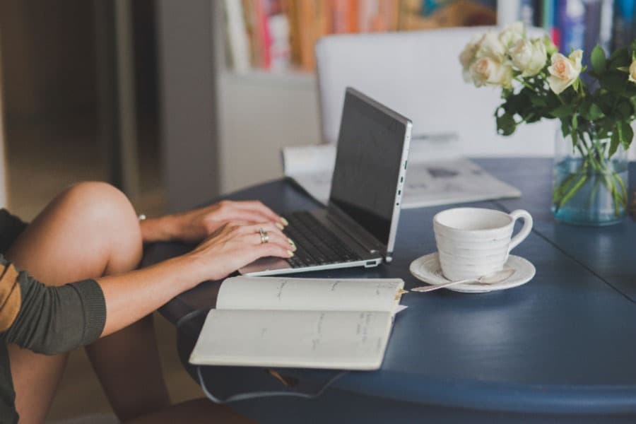 Frau sitzt vor einem Laptop mit einem Notizbuch und Kaffee