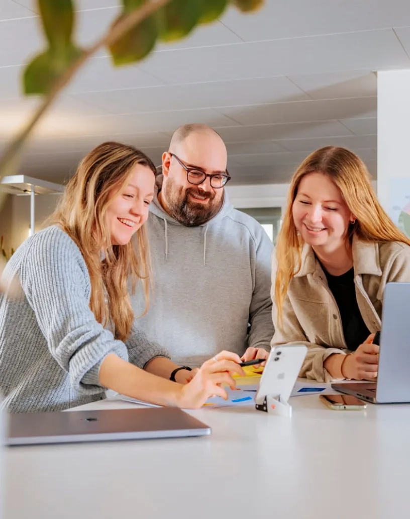 Drei Personen stehen an einem Tisch mit einem Laptop