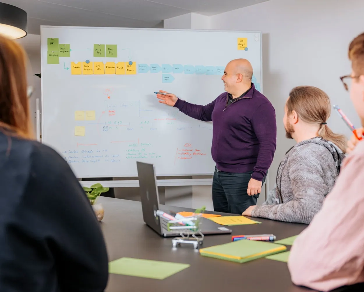 Scrum-Team hört aufmerksam dem Scrum Master im violetten Shirt zu.